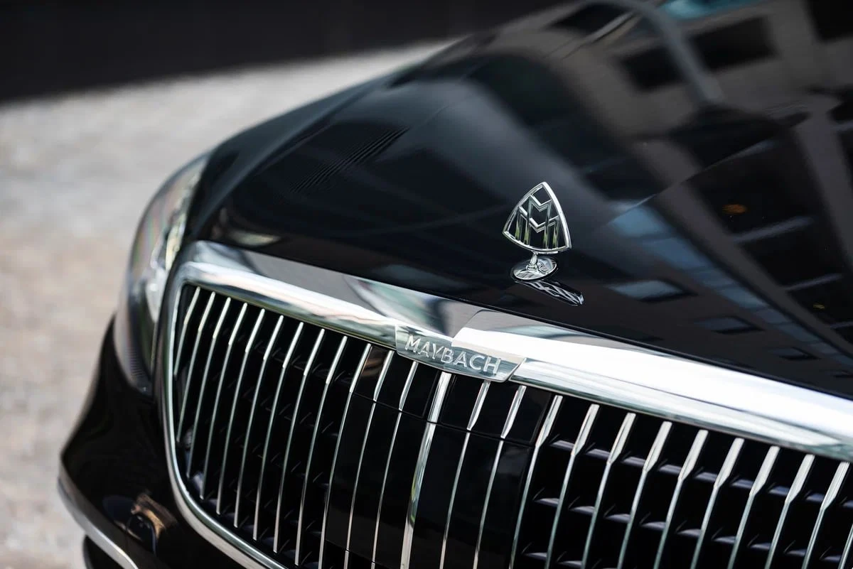 Черный Mercedes с водителем под зонтом на мокрой улице.
